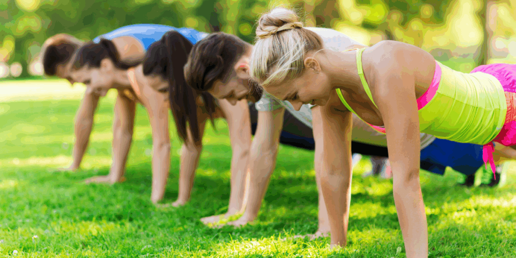 Group of people exercising by doing push ups on the grass.