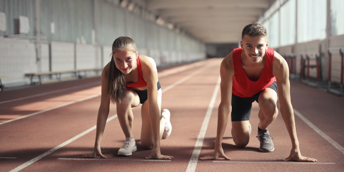 A pair of runners standing at the starting line of a running track, prepared to begin their sprint.