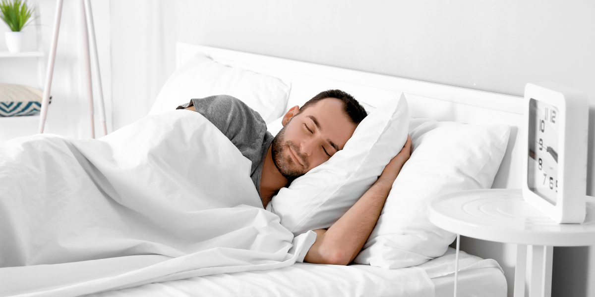 A man peacefully sleeping in bed with a white pillow.