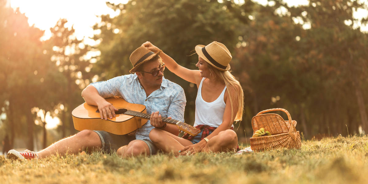 A couple playing guitar in the park, spending quality time on a picnic.