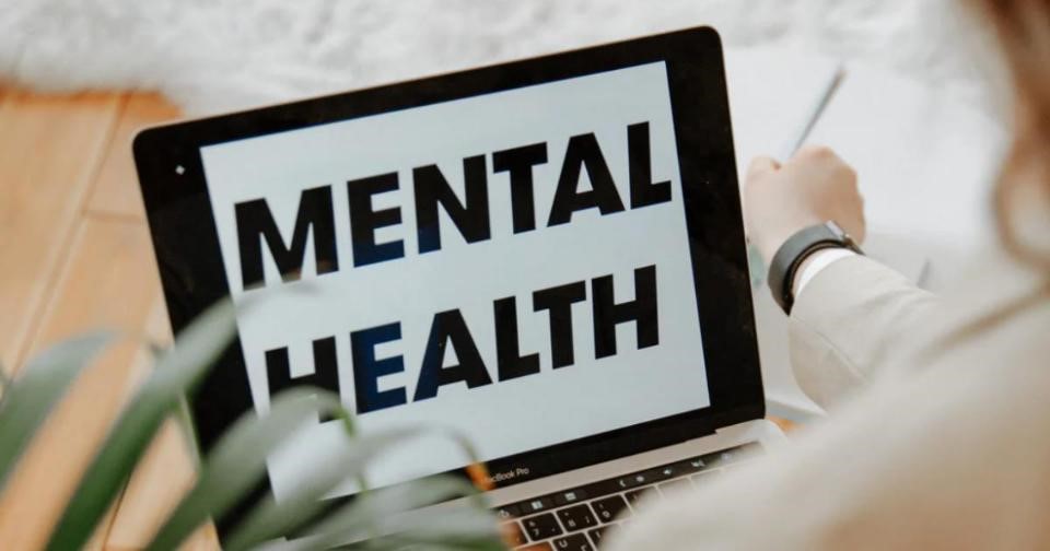 Woman sitting in front of laptop with 'mental health' displayed on screen
