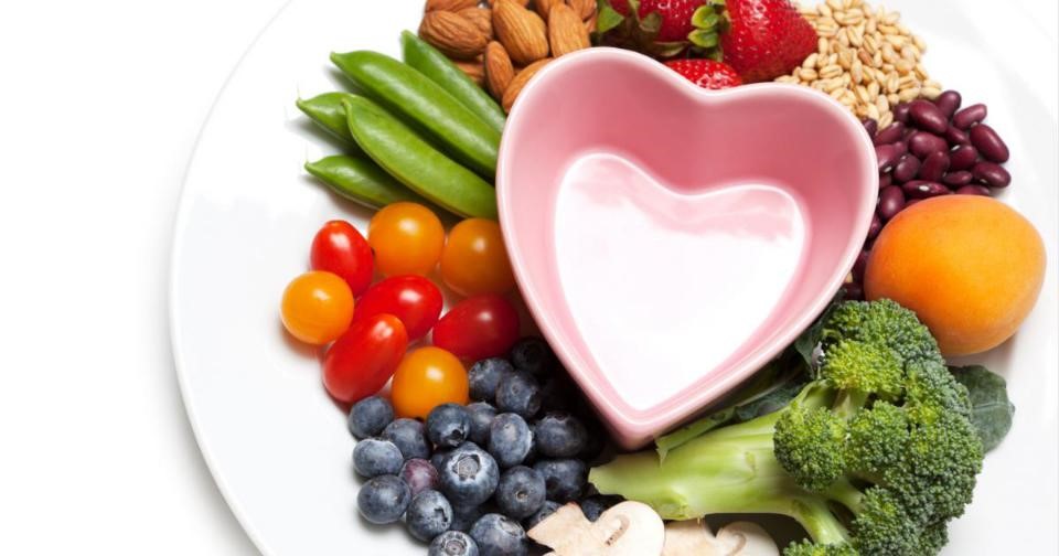 A plate with a heart-shaped bowl filled with a colorful assortment of fresh fruits and vegetables.