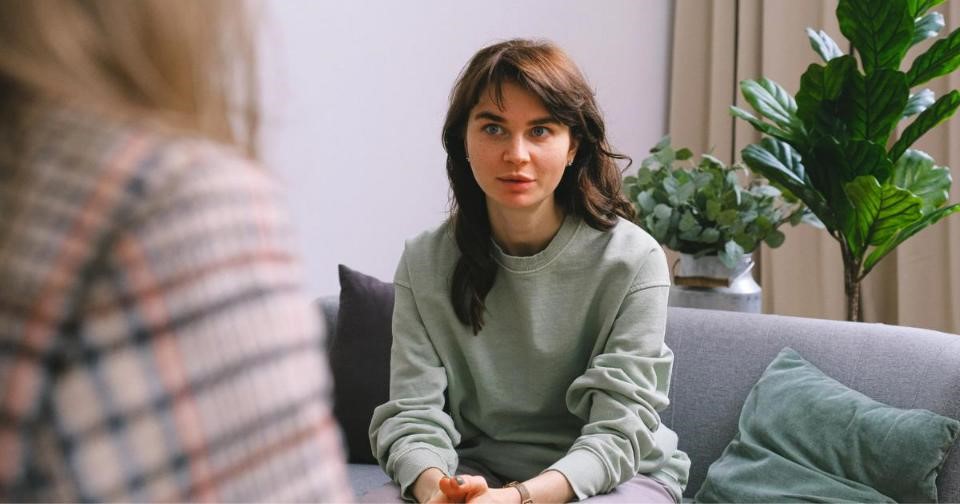 Two women engaged in a therapy session, sitting on a couch and having a conversation.