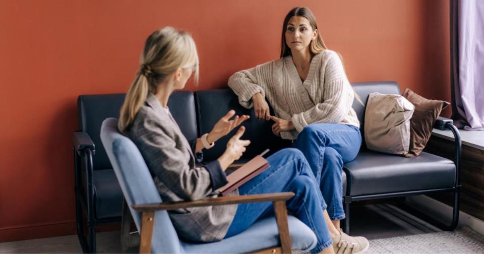 Two women on a couch, one listening attentively as psychologist explains during a therapy session.