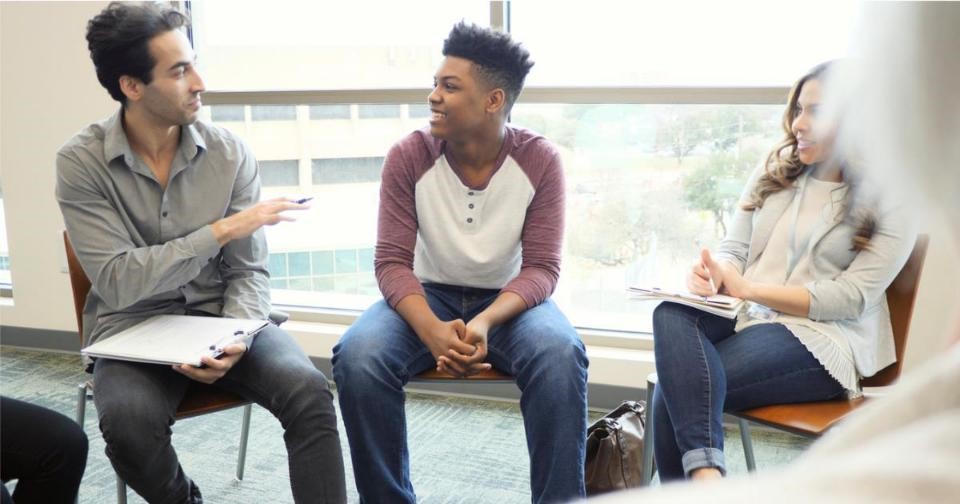 A teenager sitting in a circle with other individuals, engaging in a group therapy session.