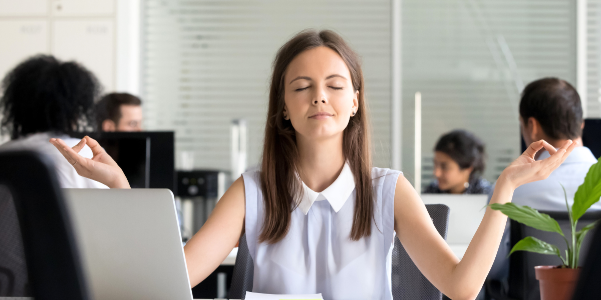 Woman calmly meditating in an office environment at her desk.